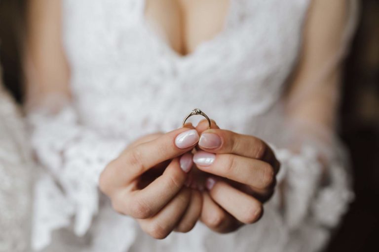 Breast of young bride dressed in wedding dress with engagement ring in hands with diamond